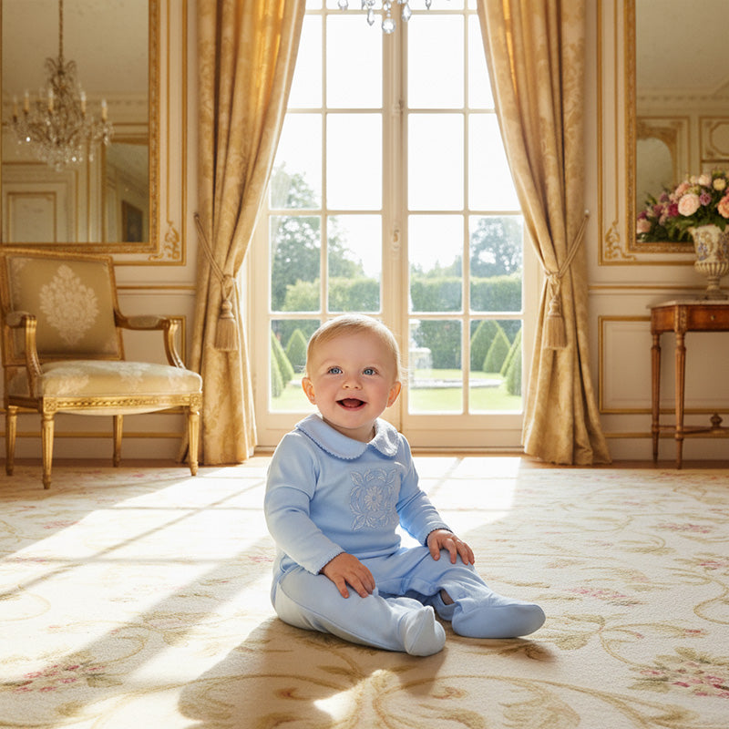 “Baby boy wearing blue embroidered babygrow with picot trim and reversible cuffs.